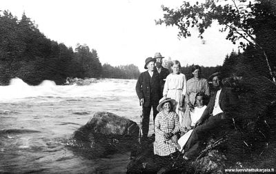 Rouhialan koski. Oikealla Antti Rapanen, vieressä istuu Anna Komi, keppi kädessä Matti Komi, vieressä Lemiltä Väinö Olkku, Olga Räikkönen vieressä nainen Penttilästä.
