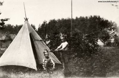 Kanneljärven kylä. Intiaanit tähtäilevät Liro pyssyillä Summan ryytimaassa. Seisomassa U Seppänen, ja I Summa maassa A Summa. Takana vas. Seppä-Sakarin paja, oikealta ent. Tahteroosin rakennus.
