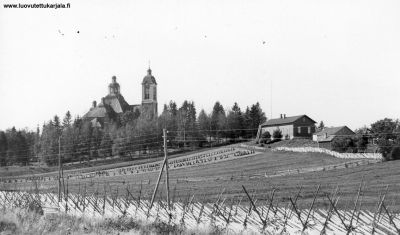 Kuva Kivennavan kuudennesta kirkosta, joka tuhoutui talvisodan alussa. Oikealla pitäjäntupa.
