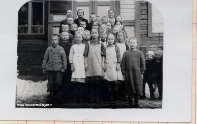 Kuvassa teksti. Kumolan koulu rakennettu 1910-1912. Sitä ennen oli vuokrahuone väliaikaisena kouluna . (Onko joku Rapo takan vasemmalla?) 
