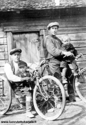 Kuvan kolmipyöräisen invapyörän istuimella on Aleksanteri Korpelainen (1889 - 1948). Alekkan molemmat jalat jouduttiin amputoimaan 1900-luvun alkupuolella paleltuman ja kuolion johdosta. Invapyörään nojaa äitini Iida Kujalan, o.s. Korpelainen (1926 - 1914) veli Toivo (1921 - 1942). Toinen pyöräilijä on Vilhelm Korpelainen, Alekkan serkku, sylissään äitini Yrjö -veli (1925 - 1943). 
  
Valokuva on otettu Aleksanterin ja hänen veljensä, äitini isän Johannes Korpelaisen pihamaalla Metsäpirtin Raajussa vuonna 1927. Meillä kuvan paperiversio on ollut aina, mutta valistunut arvaukseni on, että kuvaaja on metsäpirttiläinen, palkittu valokuvaaja Filemon Kuoppa.  
