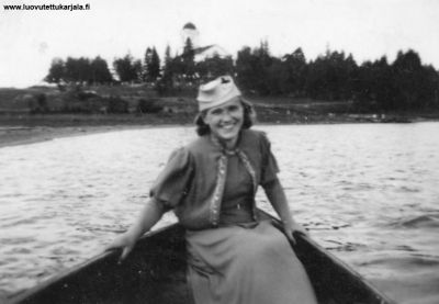 Kihupyhänä vuonna 1937 Muolaan Kirkkojärvellä otetussa kuvassa on 19-vuotias Aini Hellin Suokas myöhemmin Laakkonen. Taustalla näkyy Muolaan kirkko. 
